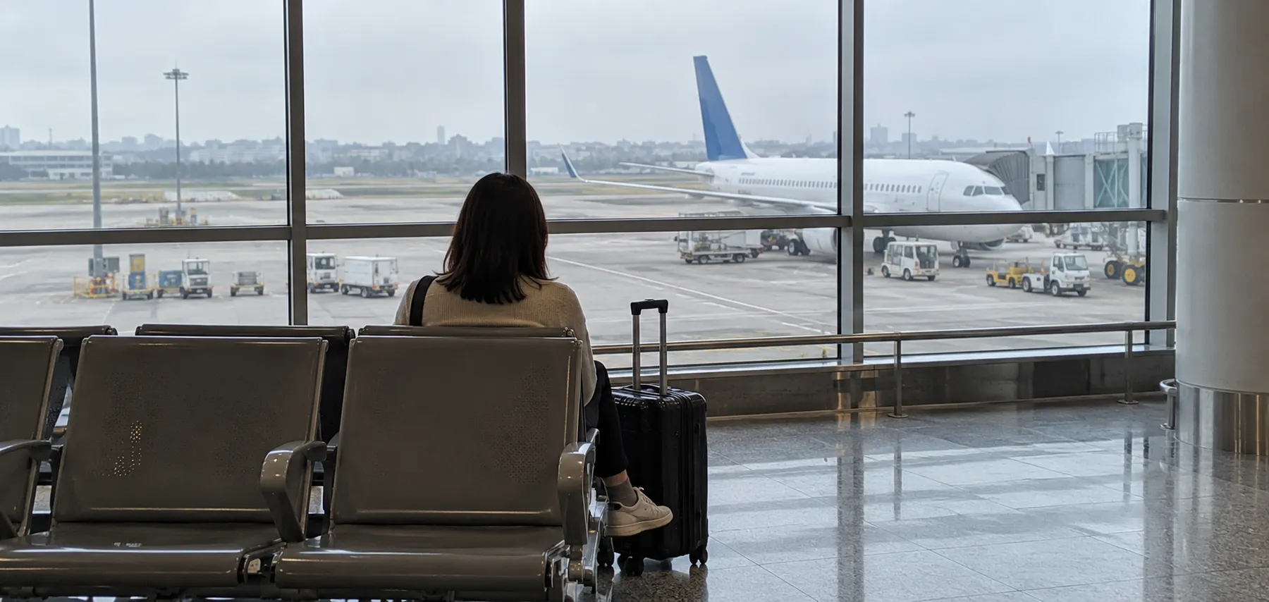 A traveler waiting at an airport gate with a carry-on suitcase